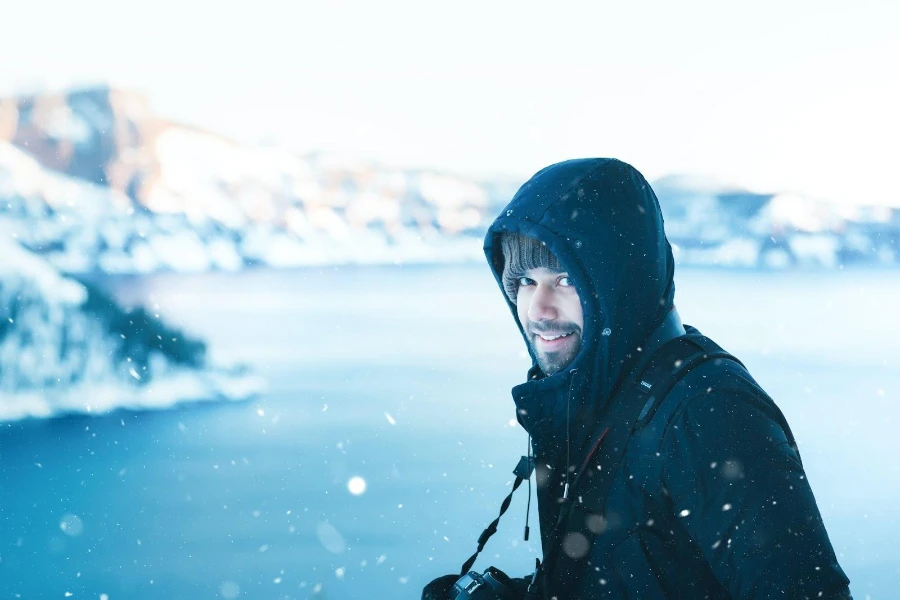 Fotógrafo de sexo masculino en la nieve que lleva una capa a prueba de tormentas