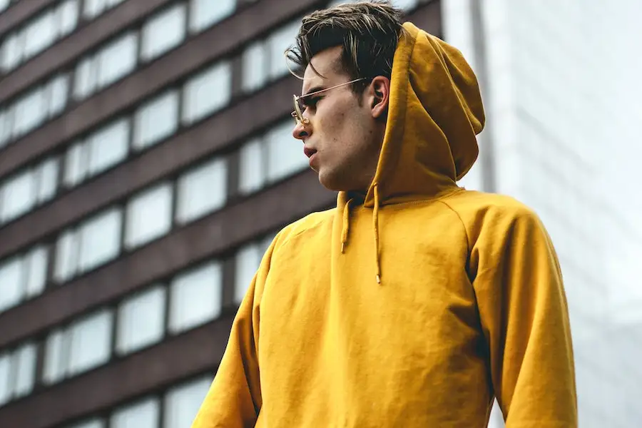 Homme avec des lunettes berçant un sweat à capuche jaune