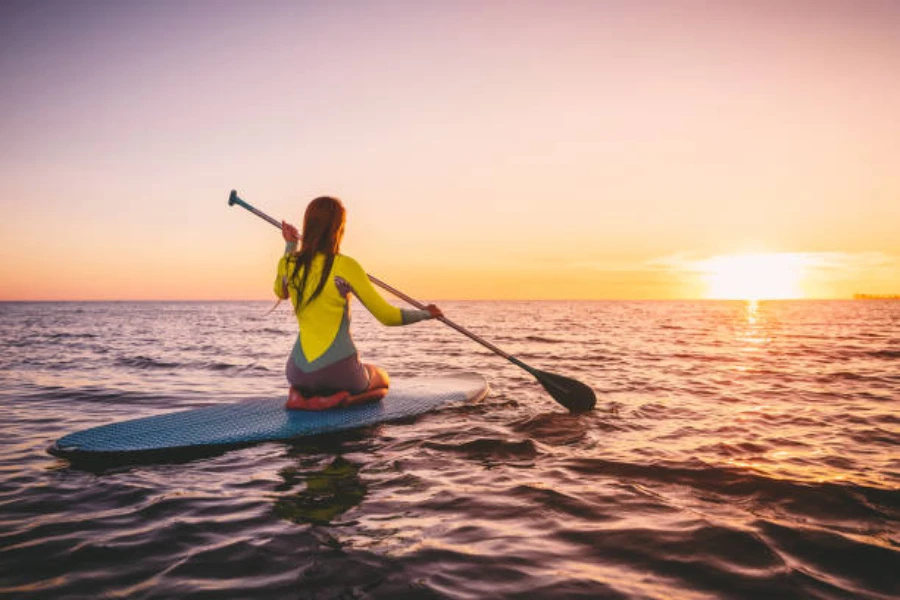 Femme agenouillée sur un paddle board tout en regardant le coucher du soleil