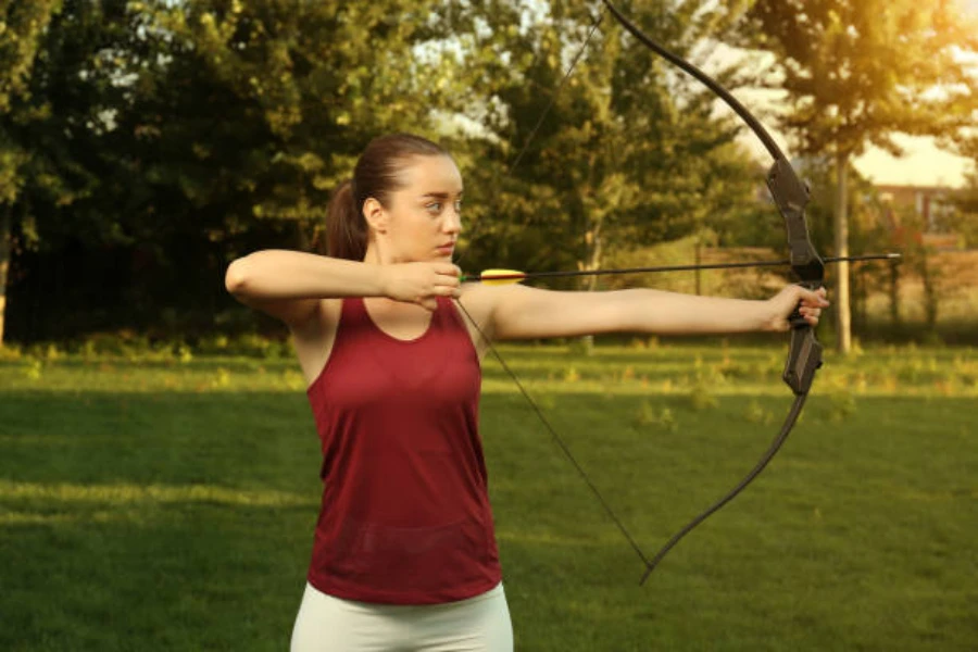 Mulher usando um arco recurvo para apontar para o alvo