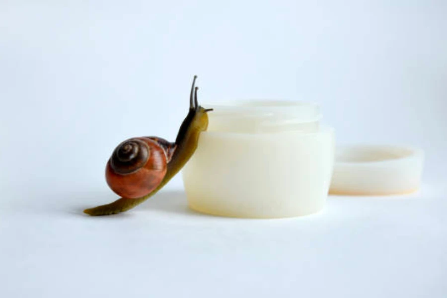 Un caracol arrastrándose junto a un frasco de crema para la piel