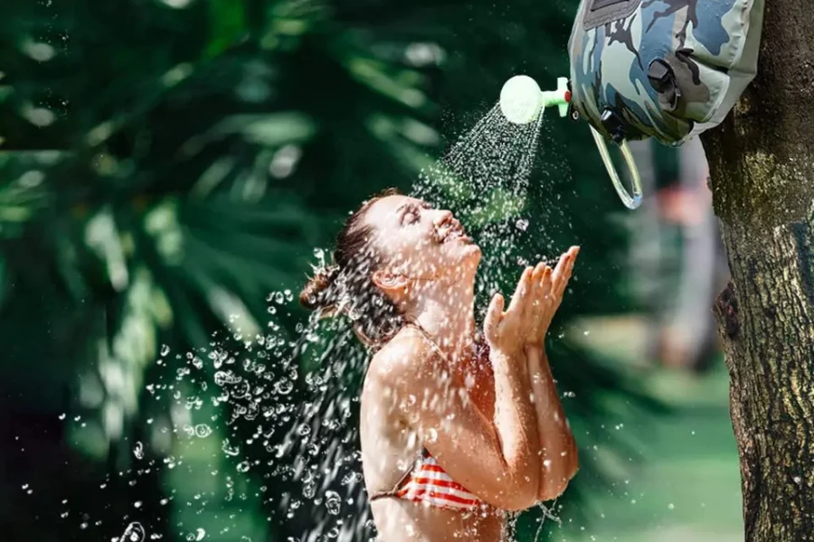 Frau im Bikini nutzt Solardusche an einem Baum