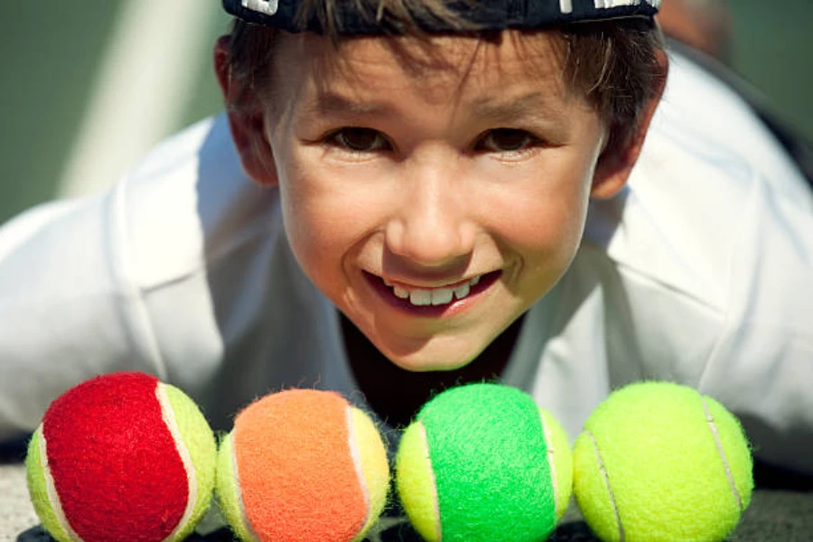 Ragazzo con quattro diversi colori di palline da tennis allineate