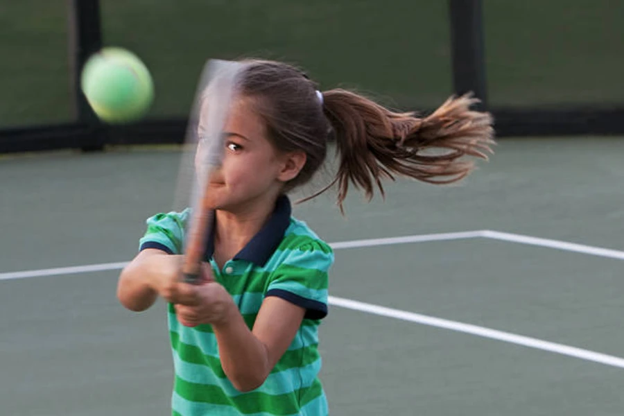 Junges Mädchen schlägt mit einem Schläger auf einen Tennisball aus grünem Filz