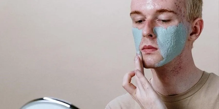 Man in brown crew-neck shirt applying anti-aging skincare face mask on his face