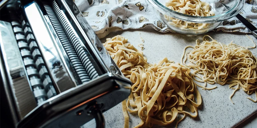 Piles of freshly made pasta on a cutting board next to a pasta machine
