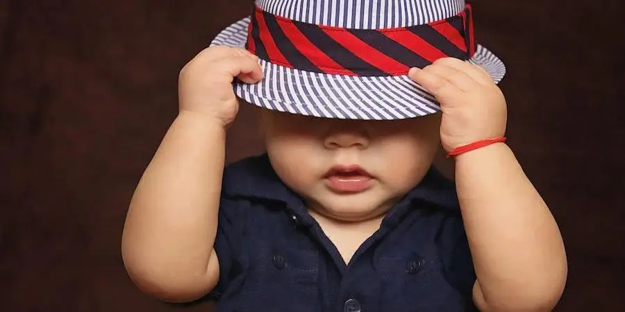 Baby wearing a blue shirt while holding stripped hat