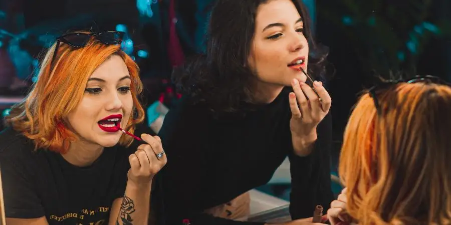 Two girls putting on makeup in a mirror