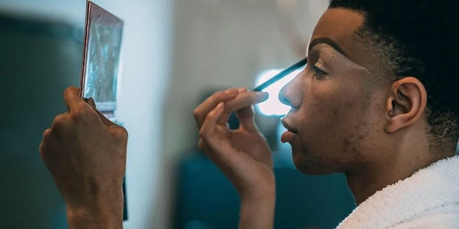 Young man applying eye makeup