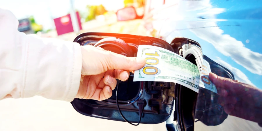 Rise in fuel price. Hand inserting a hundred dollar bill into the gas tank flap of a car.