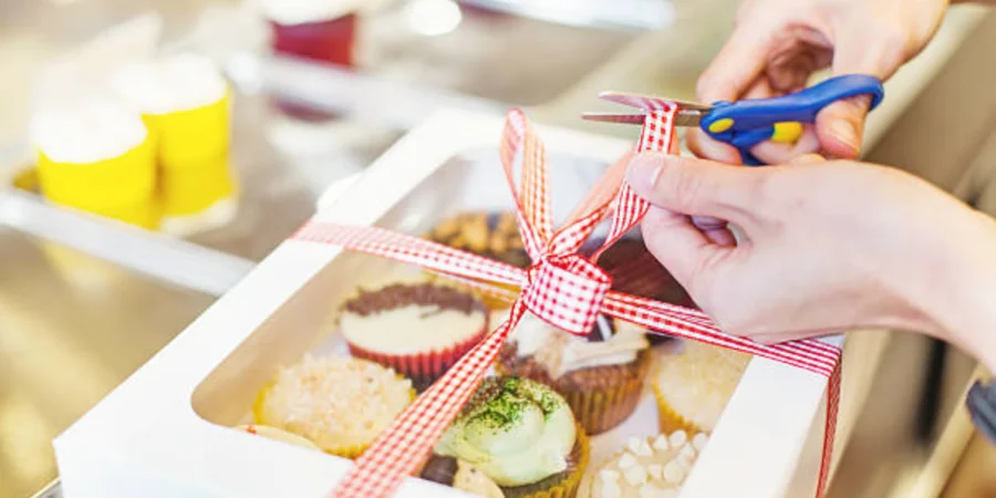 Person tying a ribbon on a box of cupcakes