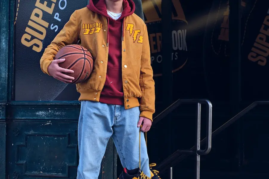 Hombre sosteniendo una pelota de baloncesto mientras usa una chaqueta marrón