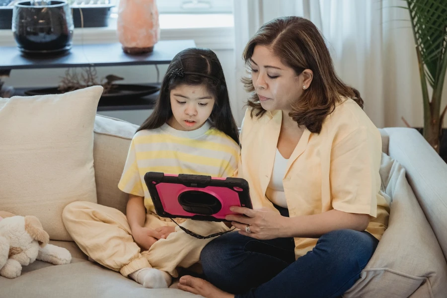 Ibu dan anak duduk di sofa sambil melihat tablet