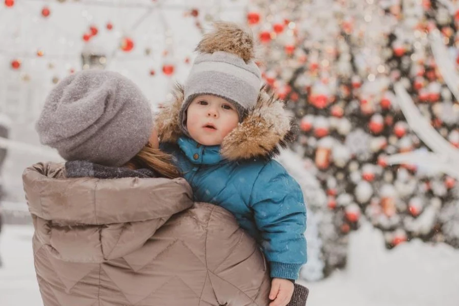 Madre che porta il bambino con cappello invernale con paraorecchie con pompon grigio