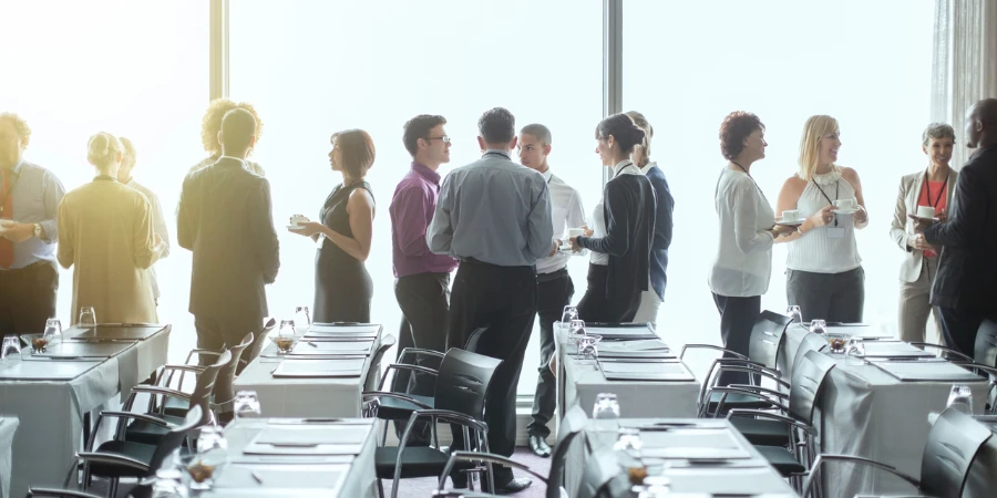 Group of people standing by windows of conference room, socializing during coffee break