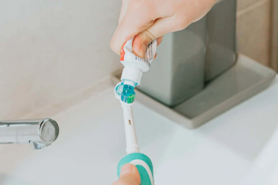 Personne ajoutant du dentifrice à une brosse à dents électrique