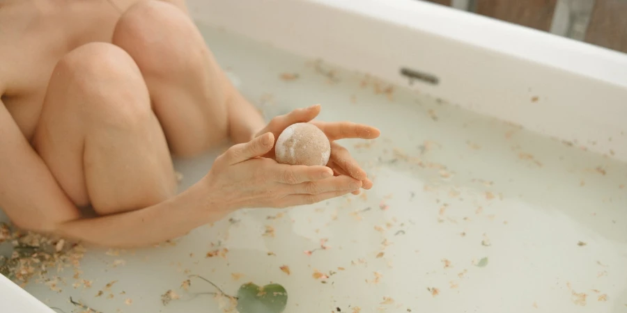 Person holding a bath bomb in milky-white bath water