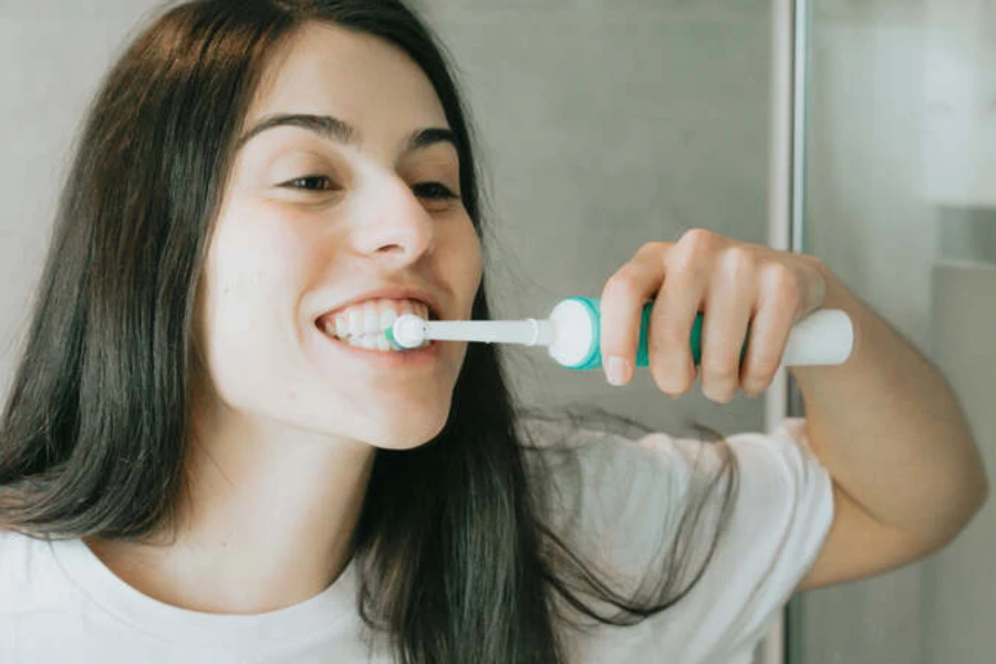 Mujer cepillarse los dientes con cepillo de dientes eléctrico