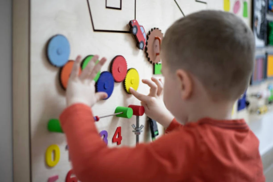 Kleiner Junge spielt mit Zahnrädern, die an einer Wand befestigt sind