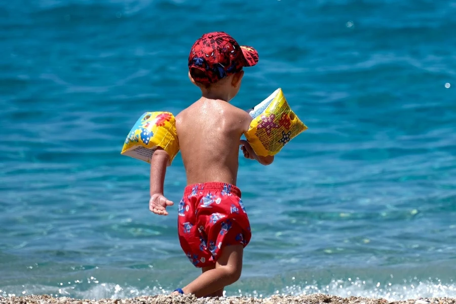 A boy in red beach shorts walking on the beach