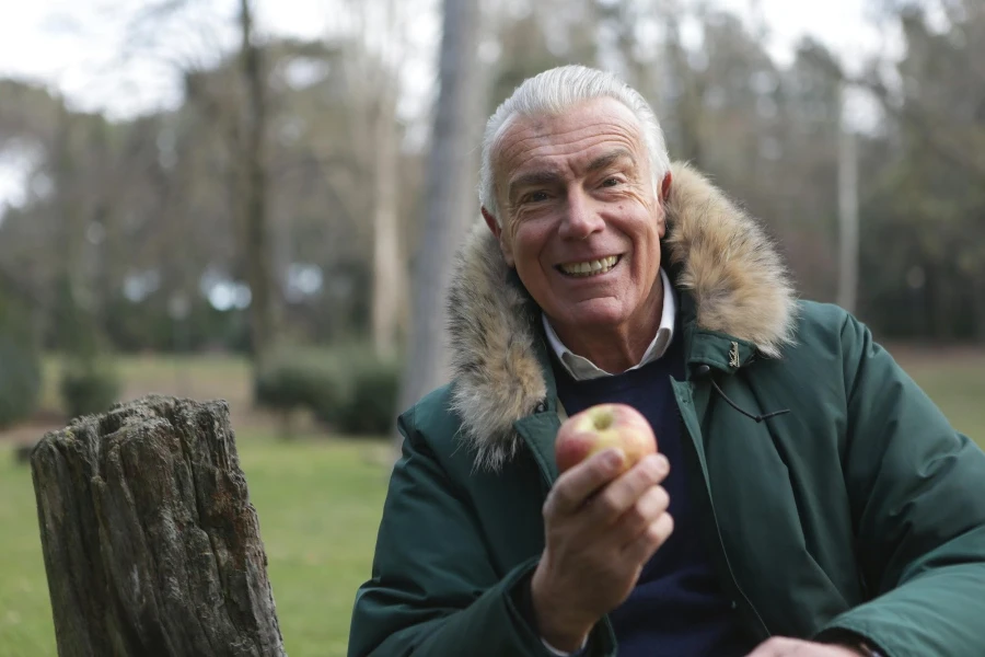 A gray-haired man holding an apple