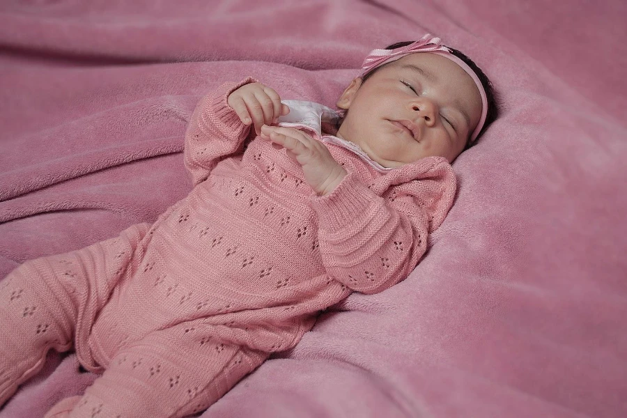 Baby girl in pink ribbed rompers lying on a bed