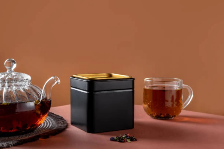 Black metal tea canister next to glass teacup and pot