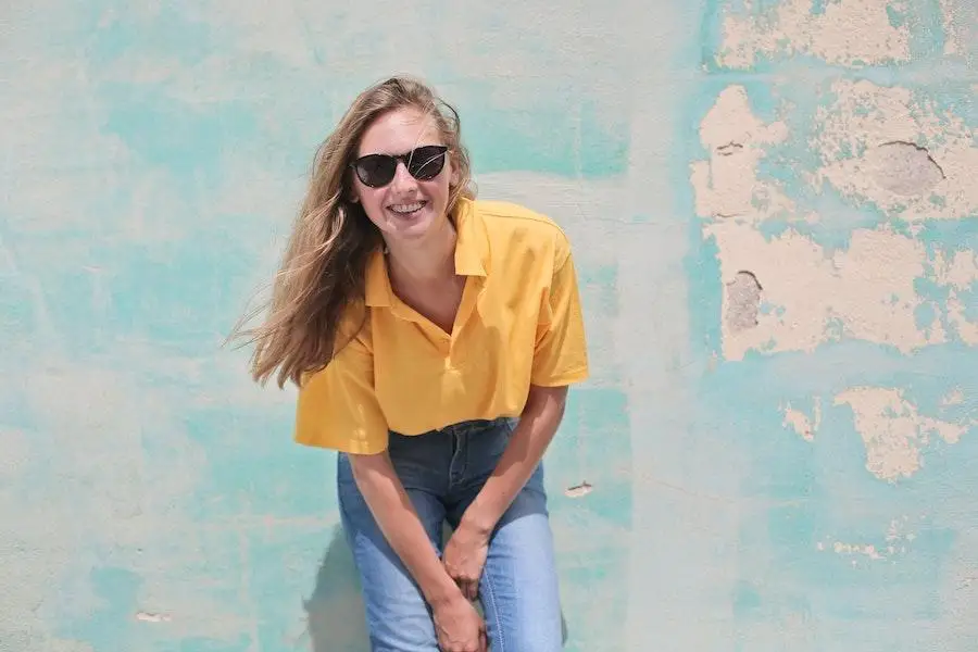 Lady in a yellow oversized shirt posing near a wall