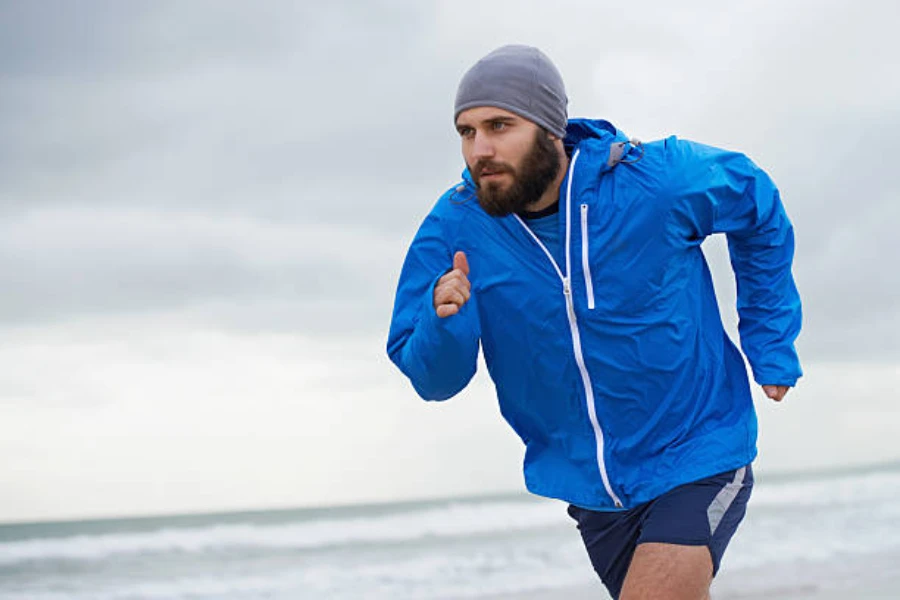 グレーのランニング ビーニー帽をかぶってビーチを走っている男性