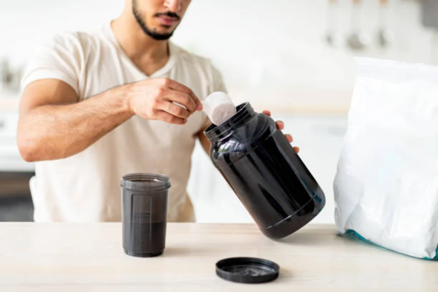 Man using scoop inside large black protein powder container