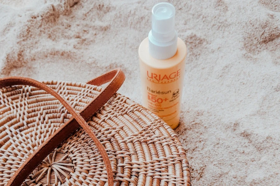 Sonnencremeflasche auf dem Sand neben einer Handtasche