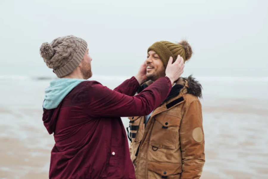 Two men wearing pom beanies on the beach in winter