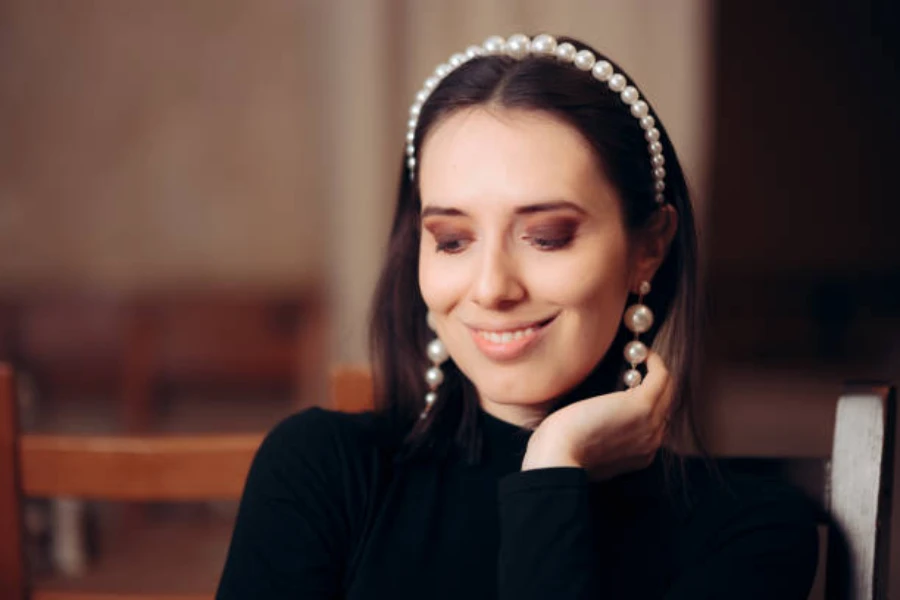 Mujer vestida de negro con aretes de perlas y diadema