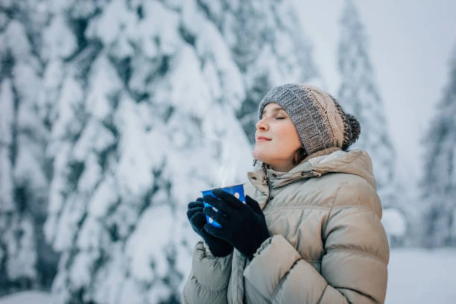 Donna nella neve che indossa berretto e cappotto con risvolto lavorato a maglia