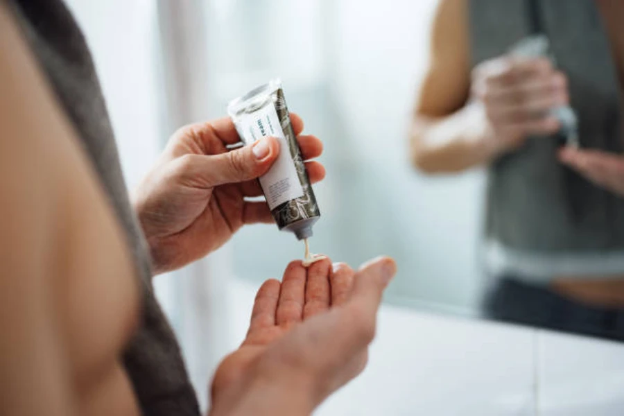 Woman squeezing aluminum tube with cream coming out