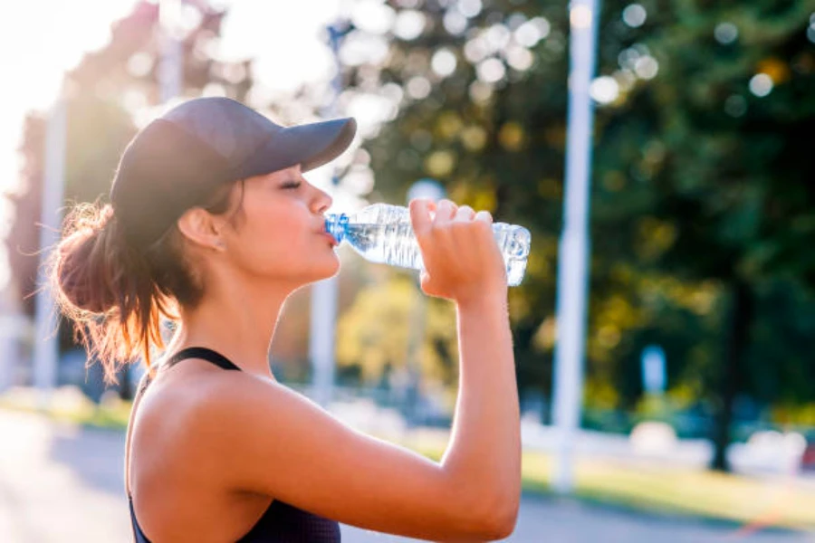 Frau trägt eine Sportmütze und trinkt Wasser