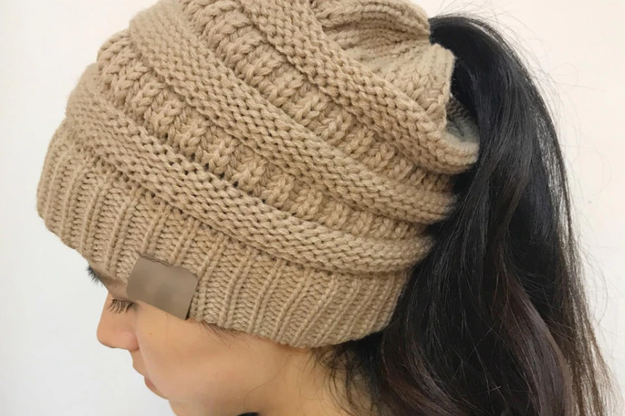Woman wearing a tan knit ponytail beanie hat