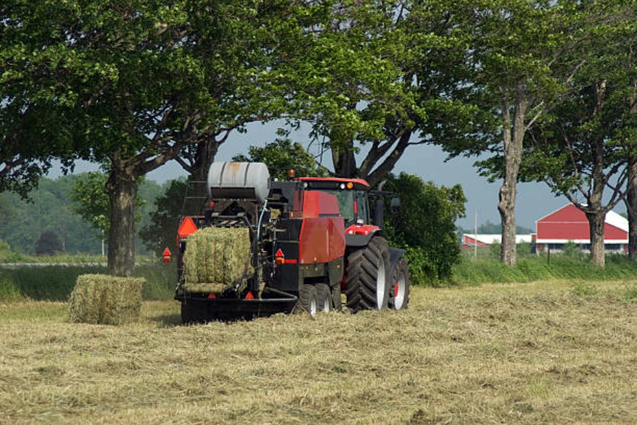 Un agriculteur pressant du foin avec une grande presse à balles carrées