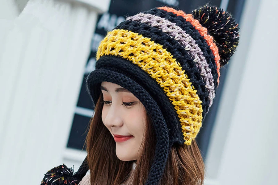 A woman wearing a knit earflap beanie with pom poms