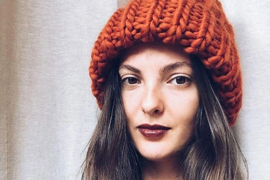 A woman wearing a rust orange chunky knit oversized beanie