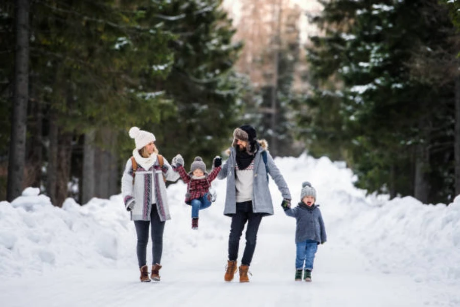 Famiglia di quattro persone che camminano attraverso la foresta in inverno indossando cappelli