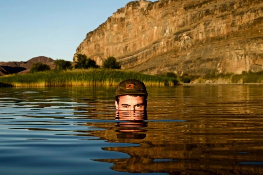 Mann im Wasser trägt Campinghut mit Lederaufnäher