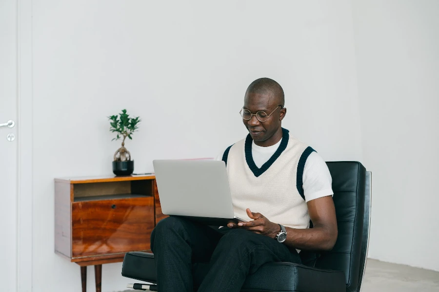 Mann sitzt auf einem schwarz gepolsterten Stuhl und benutzt einen Laptop