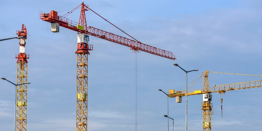 Three yellow and red tower cranes under clear blue sky