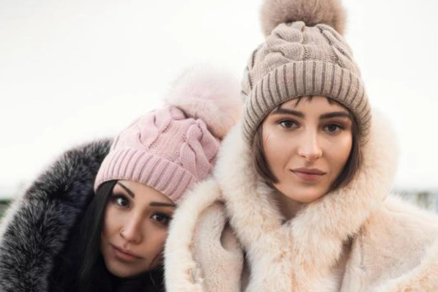 Two women wearing pink and beige cable knit beanies