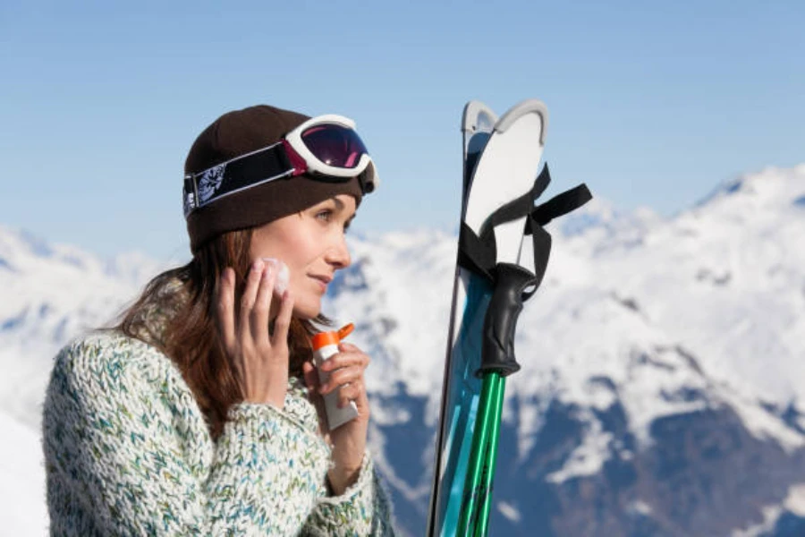 Woman on slopes wearing ski hat and applying sunscreen