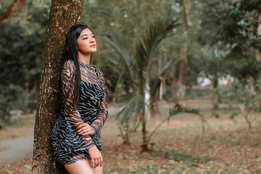 Woman wearing a minidress while posing against a tree