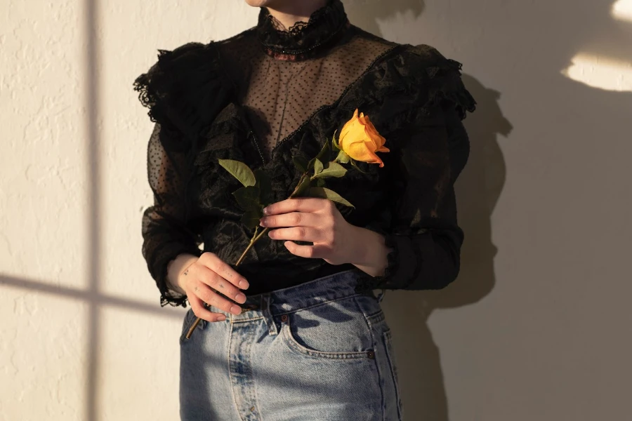 Woman wearing a sheer black blouse holding an orange flower