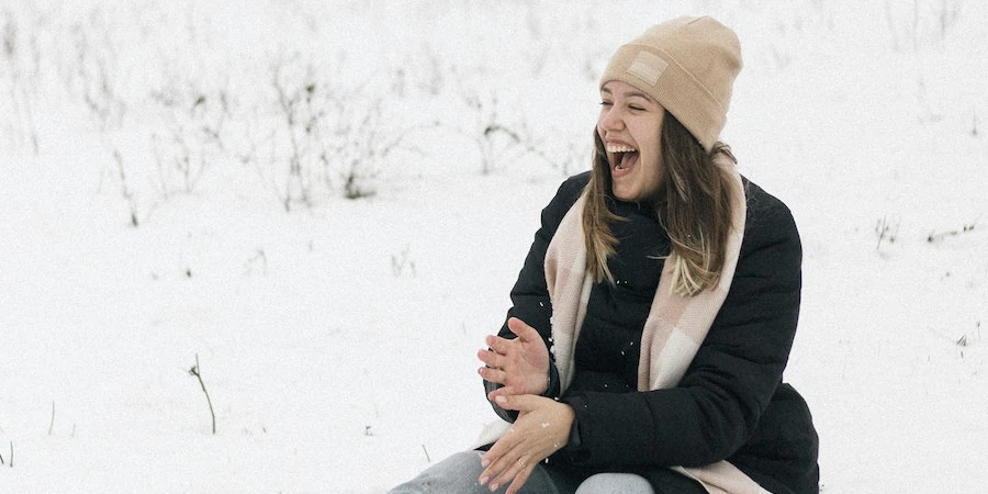 Woman wearing a winter outfit laughing and sitting on snow