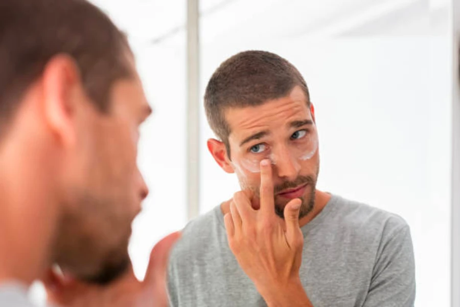 Um homem aplicando creme sob os olhos no rosto